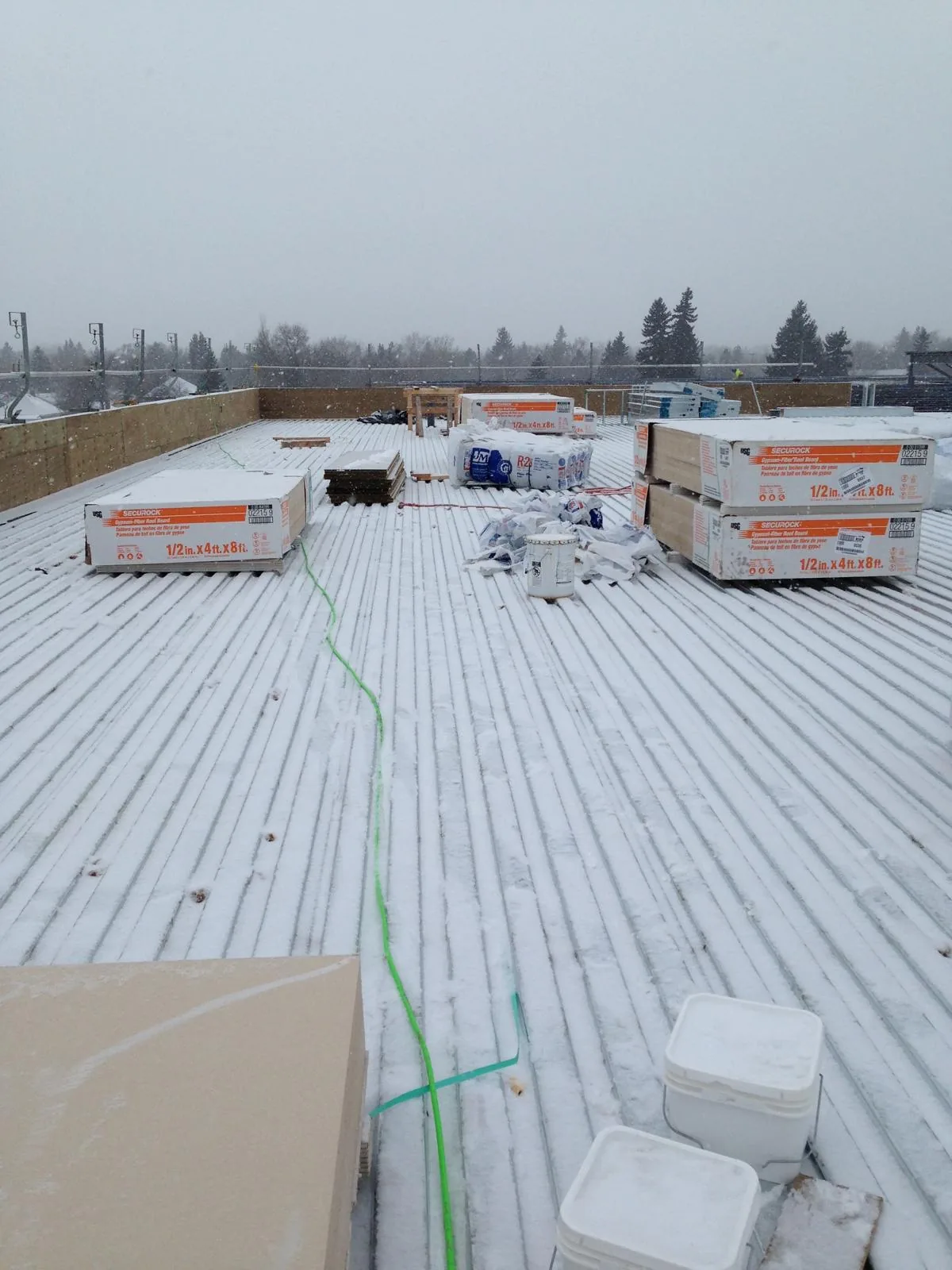 Roof board and insulation materials staged on a rooftop during heavy snowfall