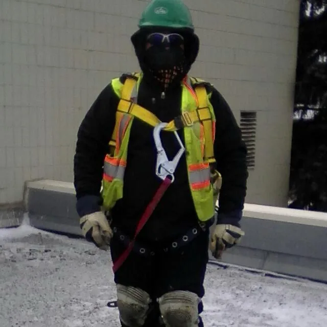 Roofer wearing full fall-arrest harness and PPE on a snowy rooftop